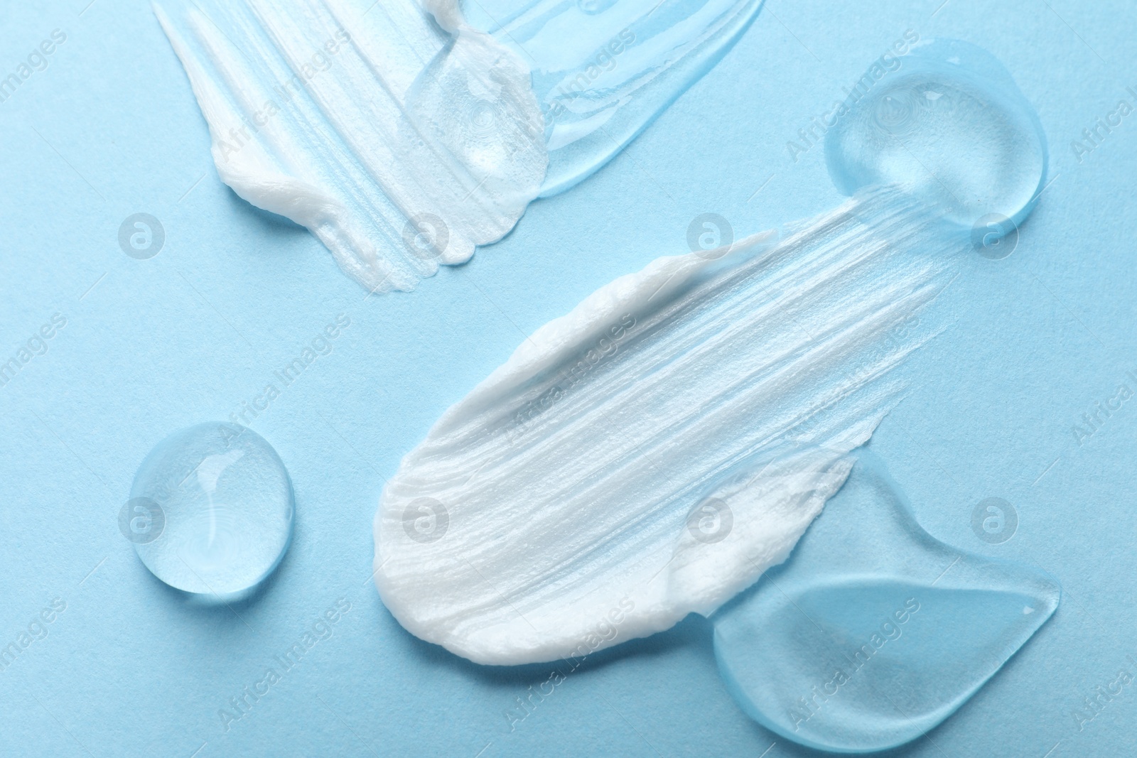 Photo of Samples of cosmetic gel and cream on light blue background, top view