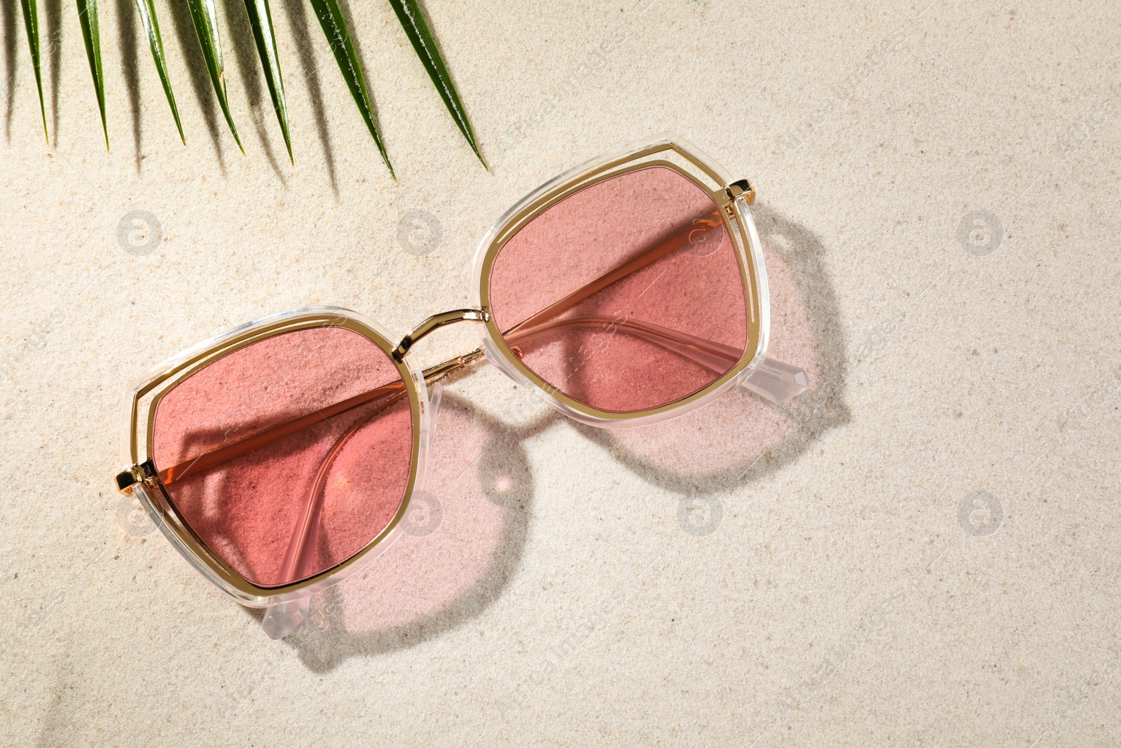 Photo of Stylish sunglasses and tropical leaf on sand, flat lay