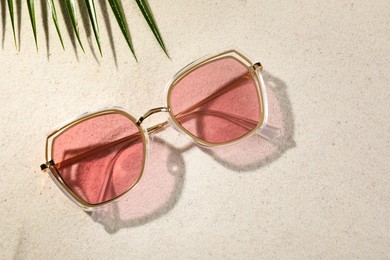 Photo of Stylish sunglasses and tropical leaf on sand, flat lay