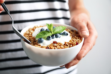 Image of Woman eating tasty granola with yogurt and blueberries for breakfast, closeup