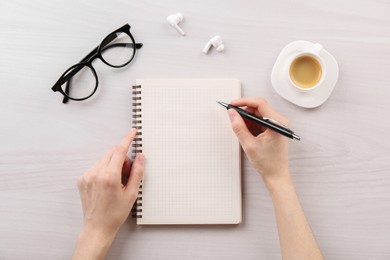 Woman with notebook and pen at white wooden table, top view. Space for text