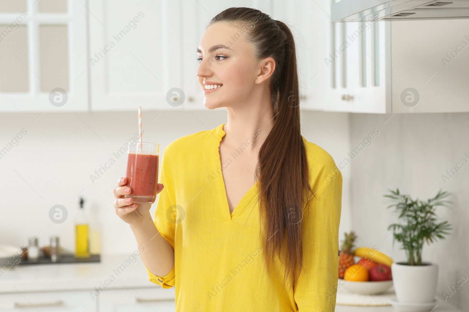 Photo of Beautiful young woman with delicious smoothie in kitchen