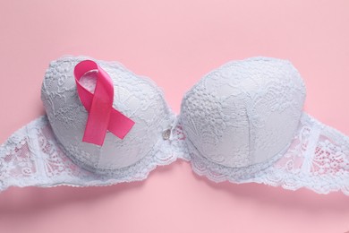 Photo of Pink ribbon and bra on color background, top view. Breast cancer awareness