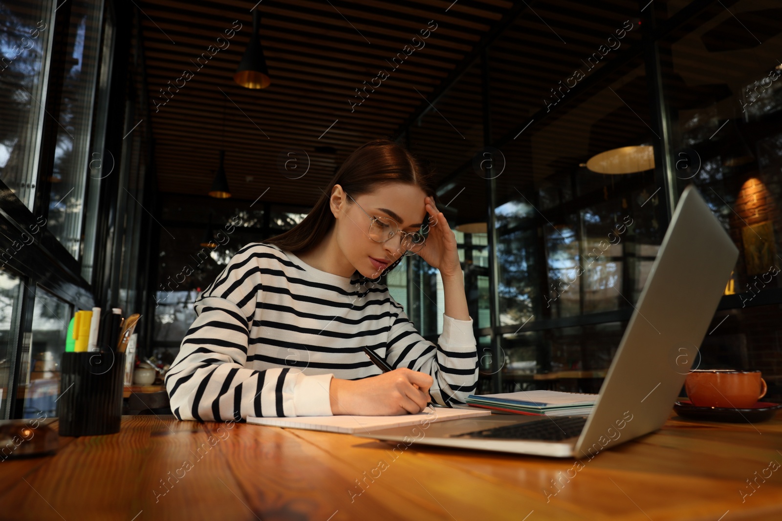 Photo of Young female student with laptop studying at table in cafe