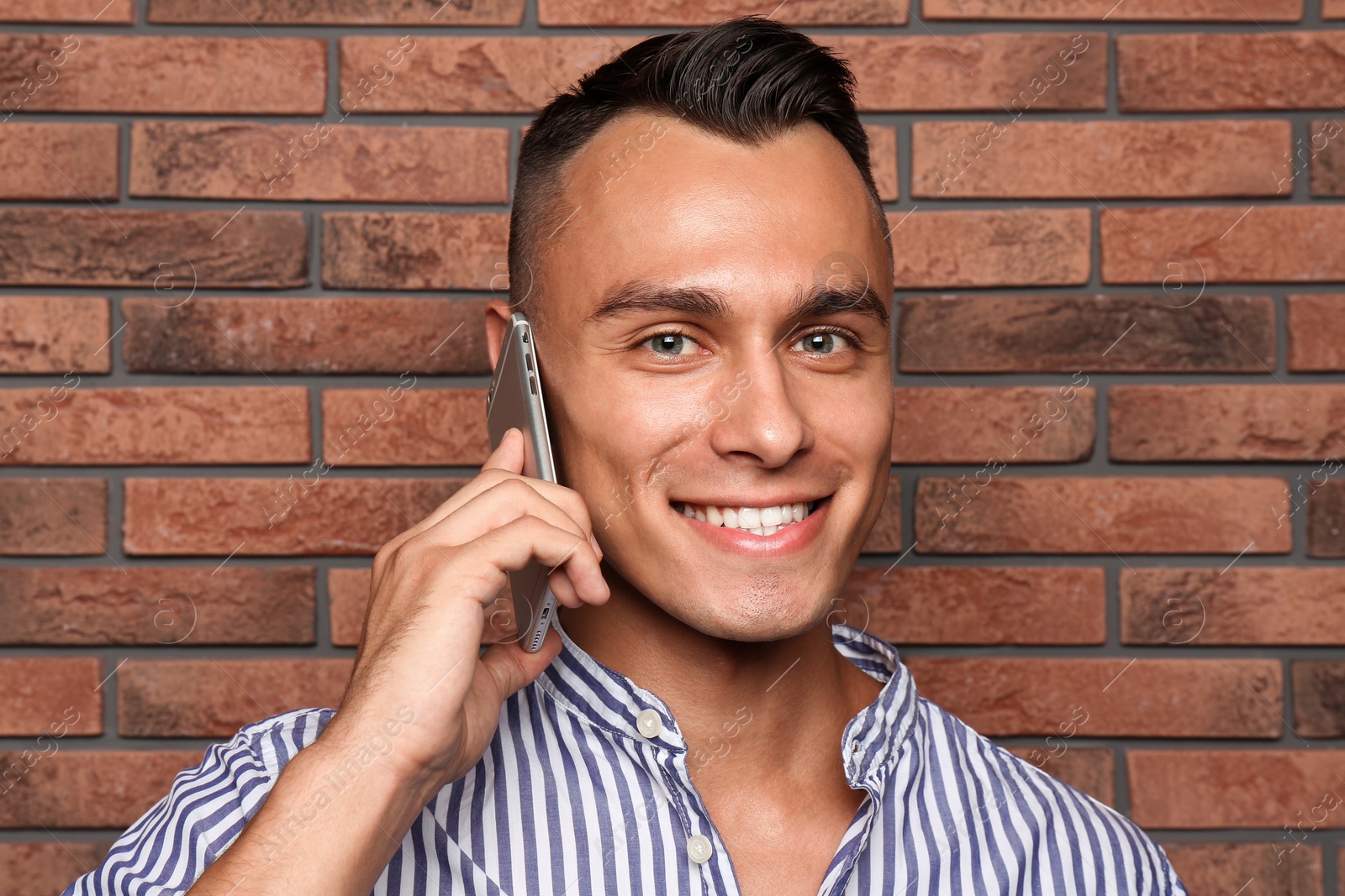 Photo of Young man talking on phone against brick wall