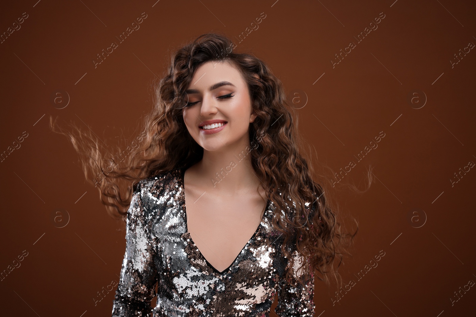 Photo of Beautiful young woman with long curly hair in sequin dress on brown background