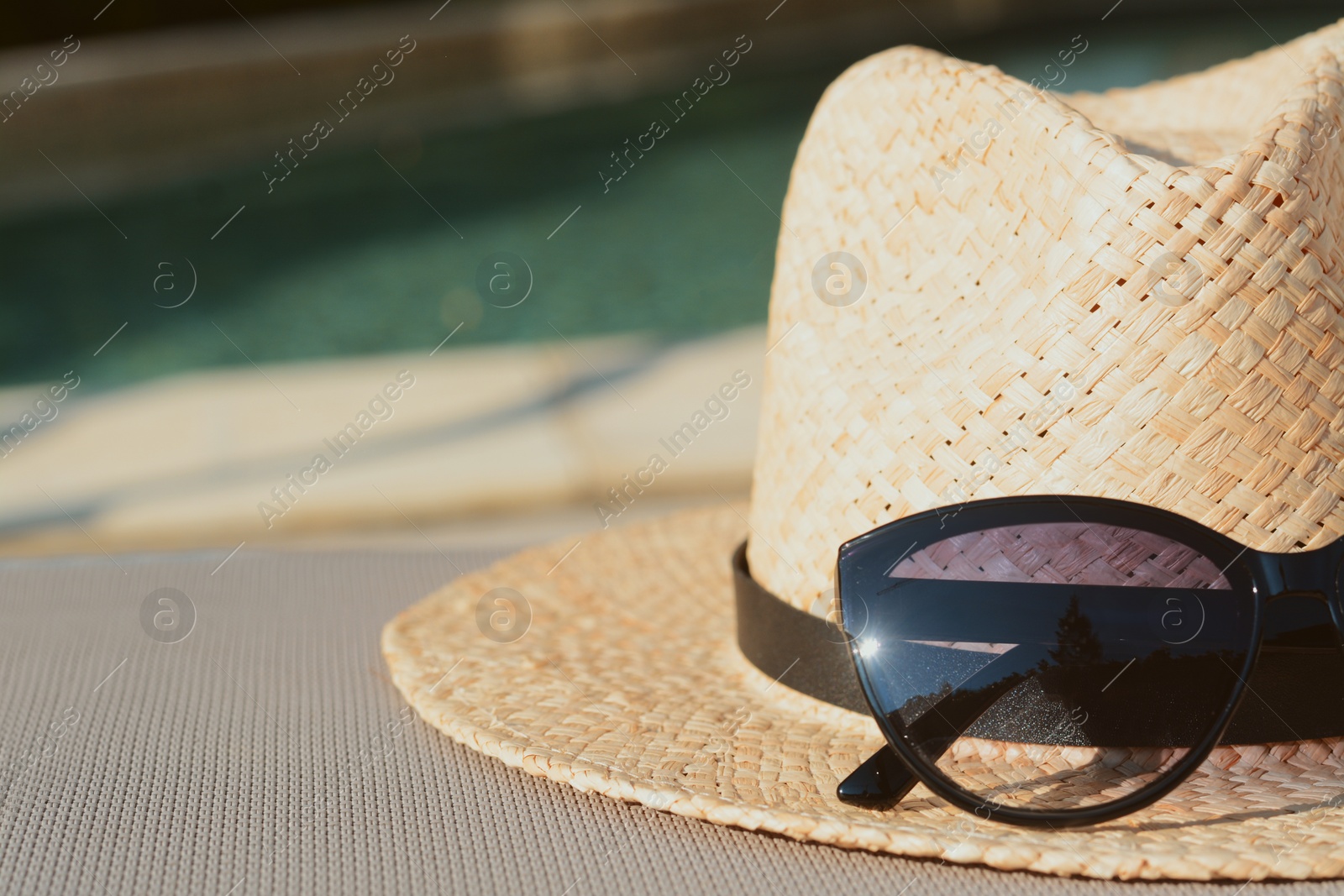 Photo of Stylish hat and sunglasses near outdoor swimming pool, closeup. Space for text