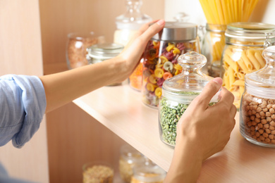 Woman taking jars of different products from wooden shelf, closeup