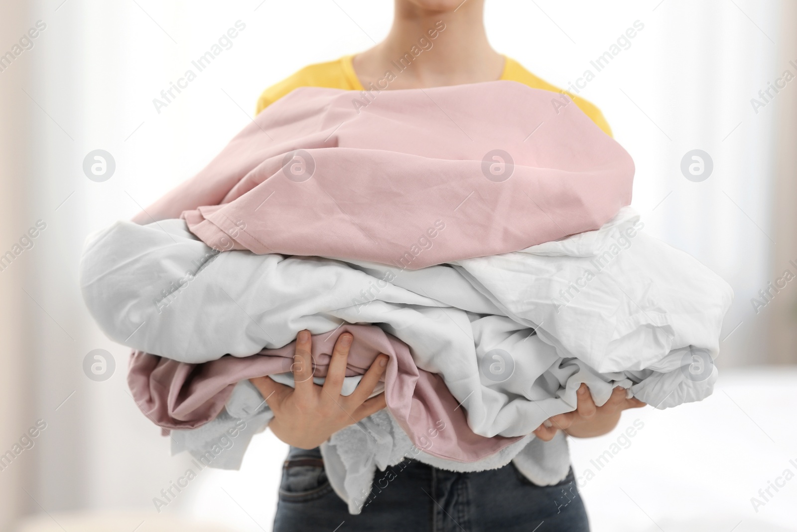 Photo of Woman holding pile of dirty laundry indoors, closeup