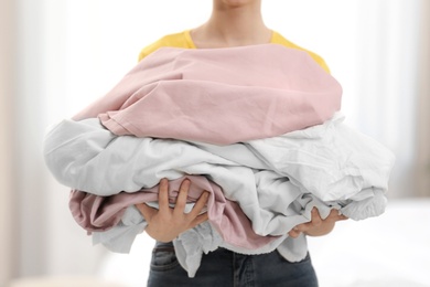 Woman holding pile of dirty laundry indoors, closeup