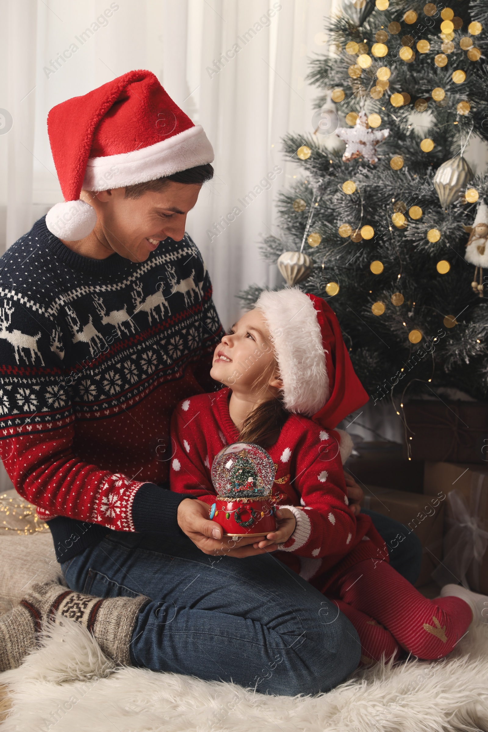 Photo of Father and daughter playing with snow globe near Christmas tree