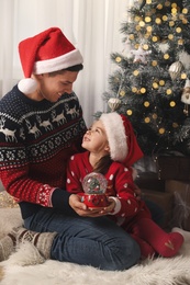 Father and daughter playing with snow globe near Christmas tree