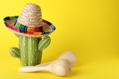 Photo of Wooden maracas and toy cactus with sombrero hat on yellow background, space for text. Musical instrument
