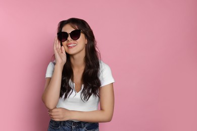 Photo of Happy beautiful woman with stylish sunglasses on pink background, space for text