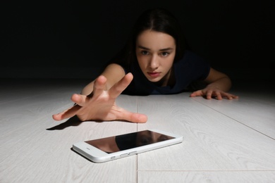 Photo of Lonely woman reaching out for smart phone on floor indoors. Internet addiction