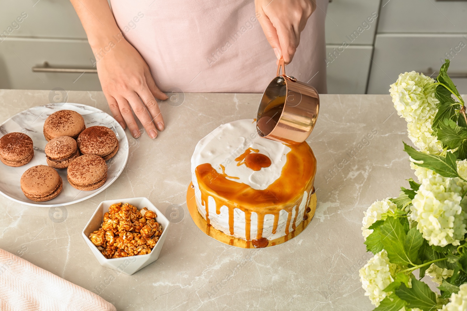 Photo of Young woman applying caramel sauce onto delicious homemade cake at table