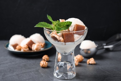 Glass bowl of ice cream with caramel candies, popcorn and mint on grey table