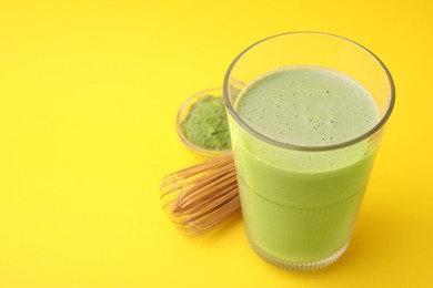 Photo of Glass of tasty matcha smoothie, powder and bamboo whisk on yellow background, closeup. Space for text