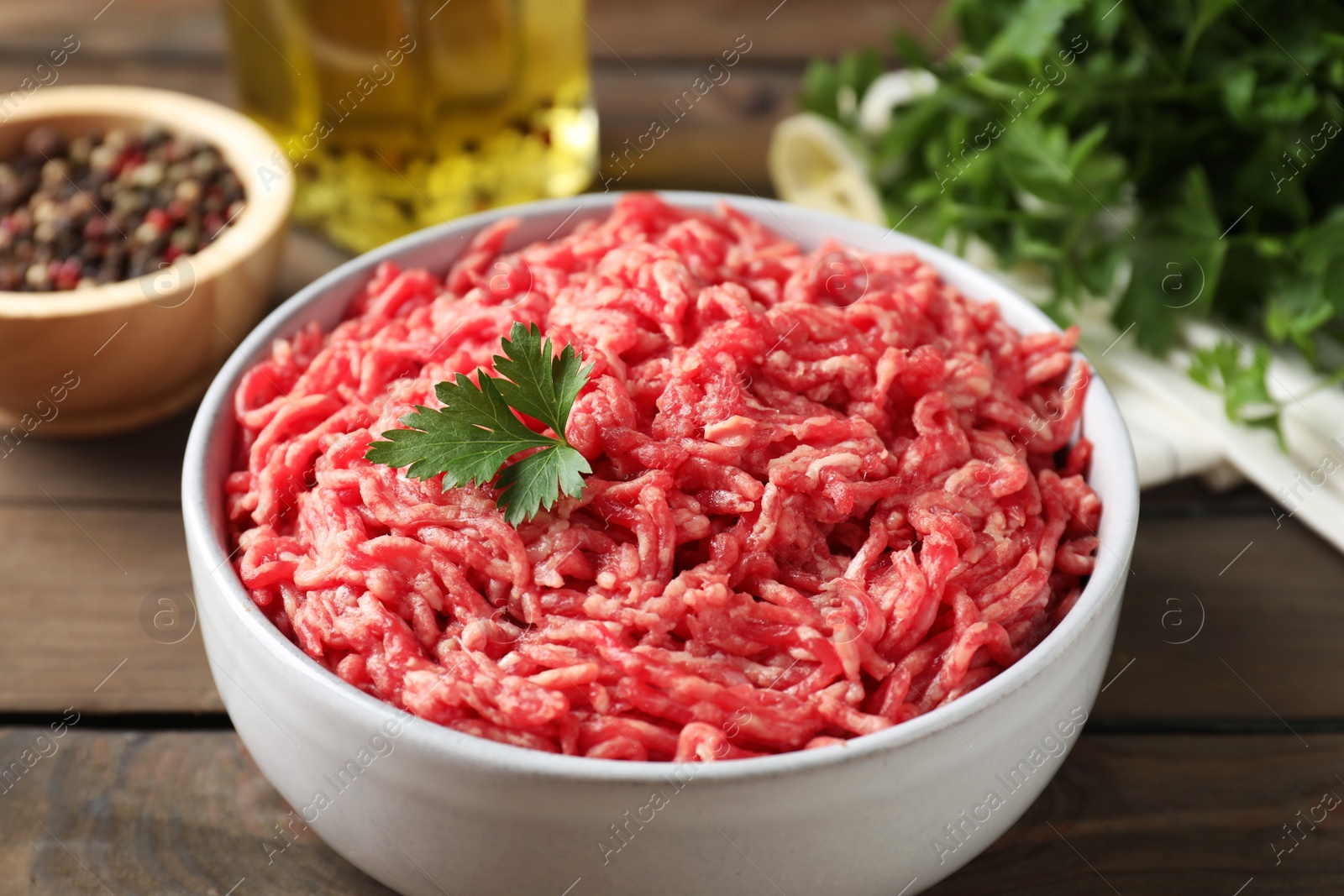 Photo of Raw ground meat in bowl, parsley, spices and oil on wooden table, closeup