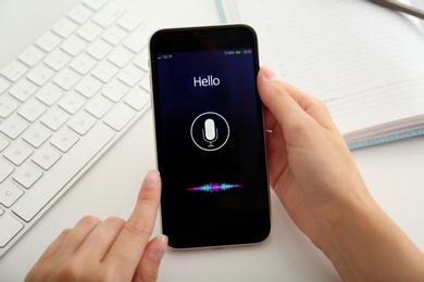 Woman using voice search on smartphone at white table, closeup