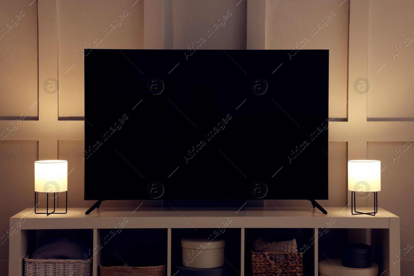 Photo of Modern TV and lamps on cabinet near white wall indoors. Interior design