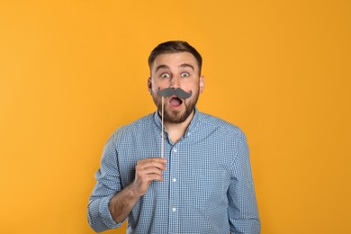 Emotional man with fake mustache on yellow background