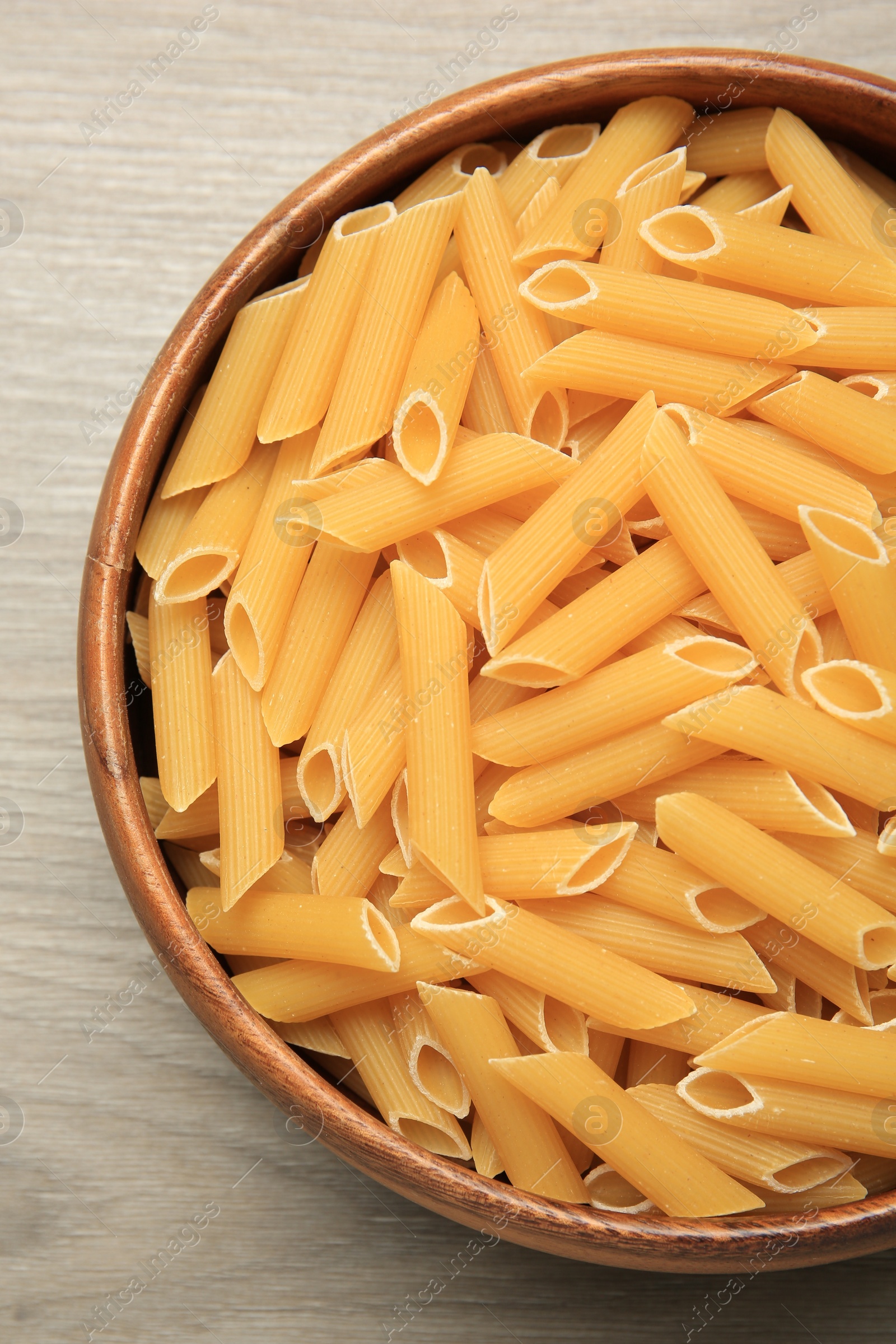 Photo of Raw penne pasta in bowl on light grey wooden table, top view