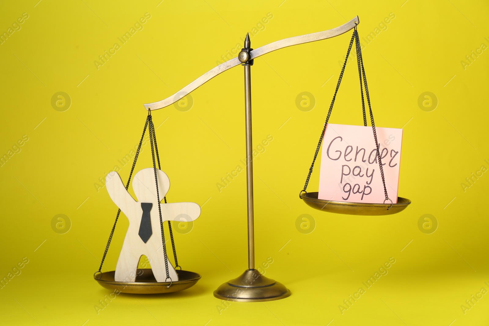 Photo of Gender pay gap. Wooden figure of man and paper note on scales against yellow background