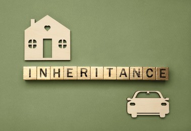 Photo of Word Inheritance made with wooden cubes, house and car models on green background, flat lay