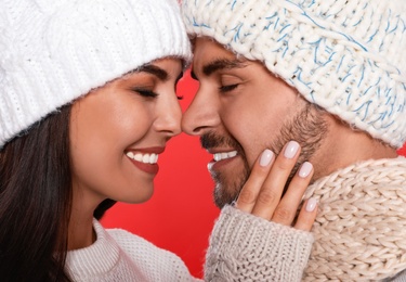 Photo of Lovely young couple in knitted hats on red background, closeup. Christmas celebration
