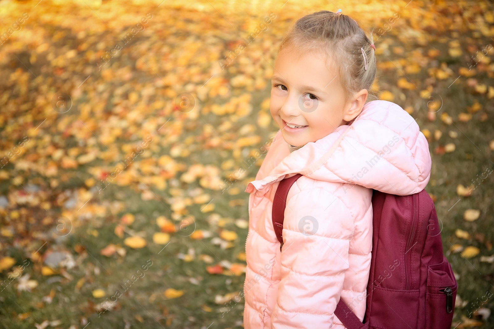 Photo of Cute little girl with backpack in park on autumn day. Space for text