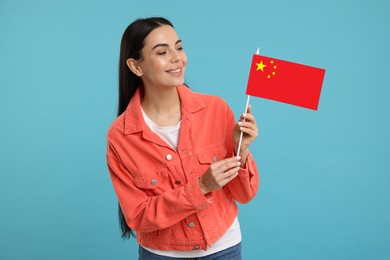 Image of Happy young woman with flag of China on light blue background