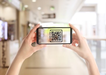 Image of Woman holding smartphone with QR code on screen in store, closeup