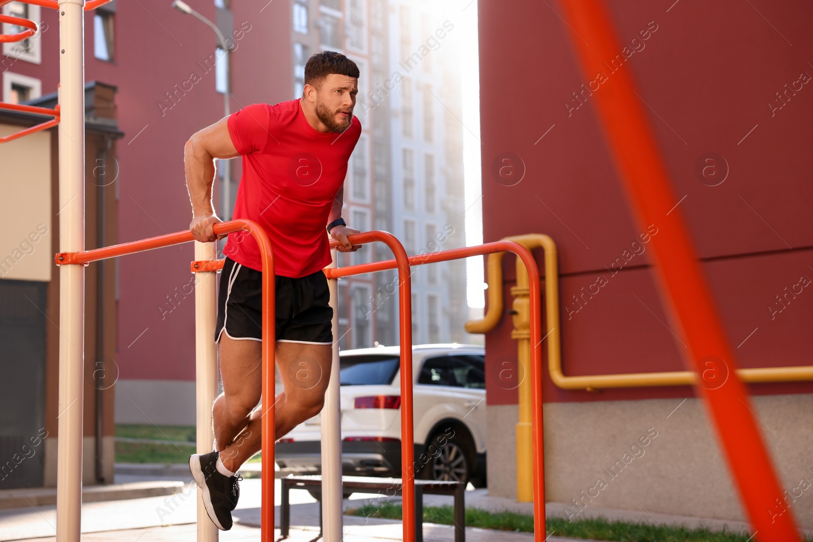 Photo of Man training on parallel bars at outdoor gym on sunny day