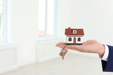 Real estate agent holding house model and key on blurred background, closeup