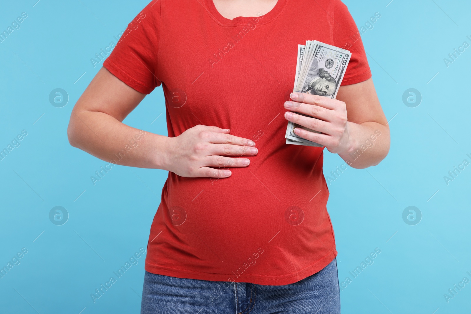 Photo of Surrogate mother. Pregnant woman with dollar banknotes on light blue background, closeup