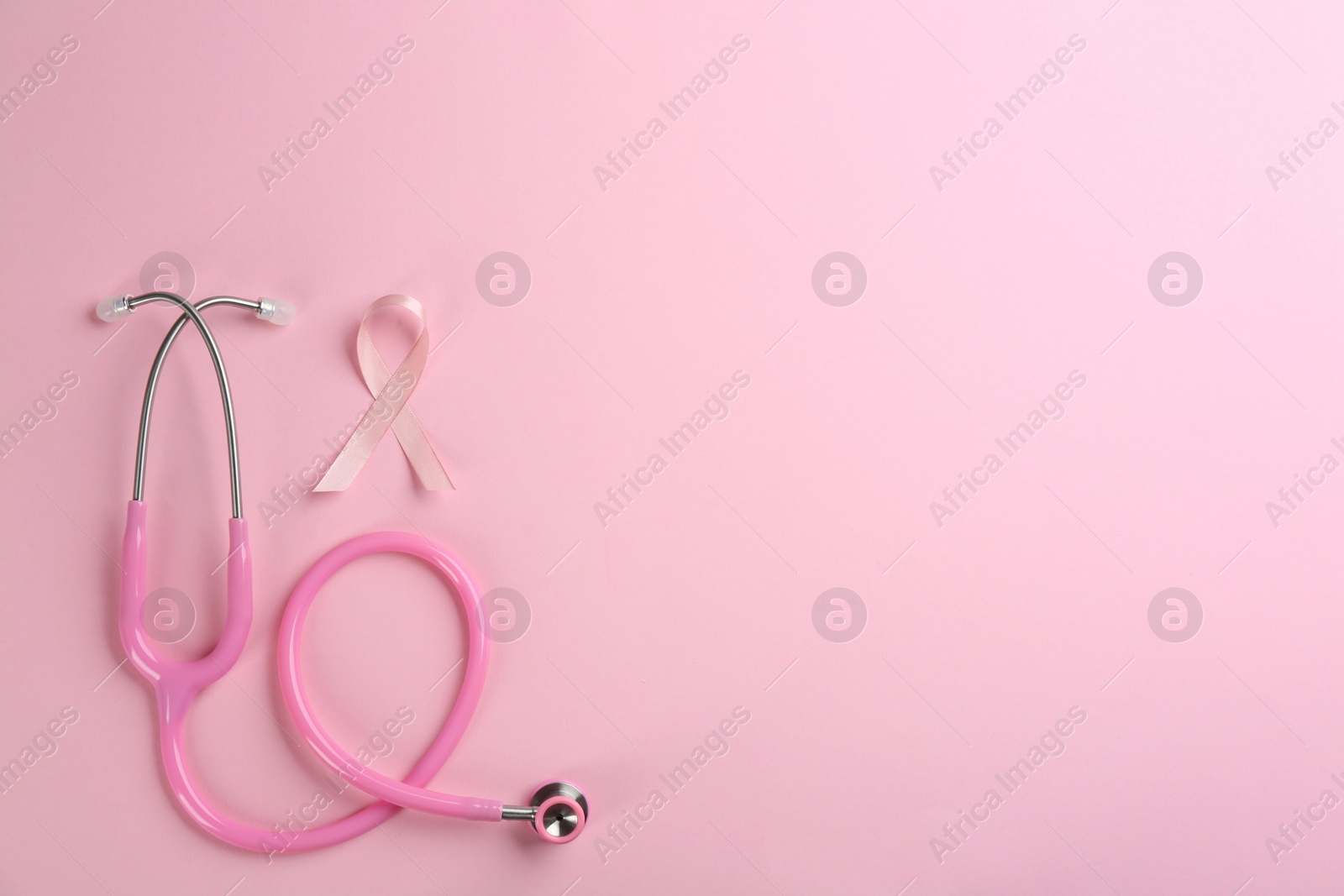 Photo of Pink ribbon as breast cancer awareness symbol and stethoscope on color background, flat lay. Space for text