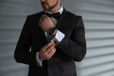 Man wearing stylish suit and cufflinks near white wall, closeup