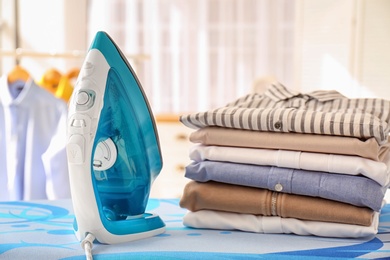 Photo of Stack of clean clothes and iron on board indoors