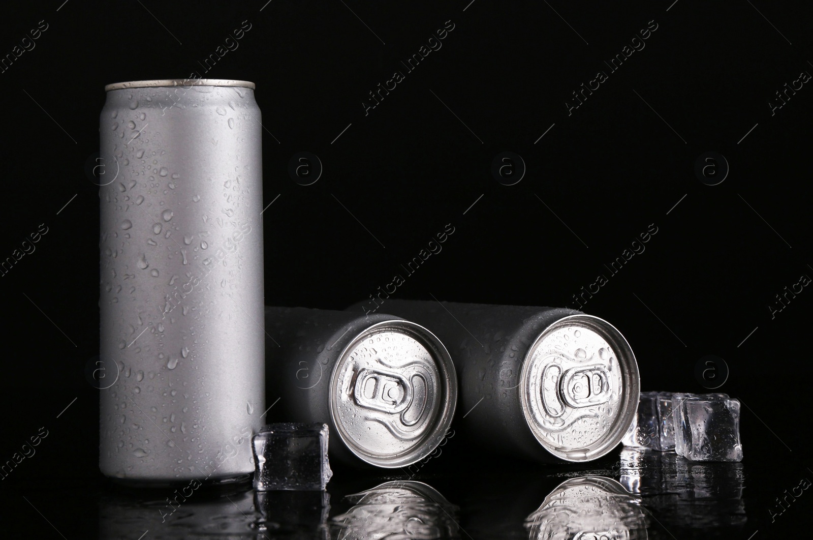 Photo of Energy drinks in wet cans and ice cubes on black background