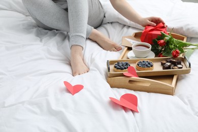 Photo of Tasty breakfast served in bed. Woman with gift box, tea, desserts and flowers at home, closeup