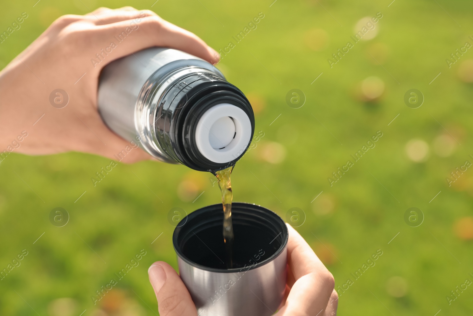 Photo of Woman pouring hot drink from thermos into cap outdoors, closeup