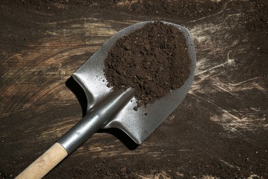 Photo of Metal shovel with fertile soil on dirty wooden surface, top view