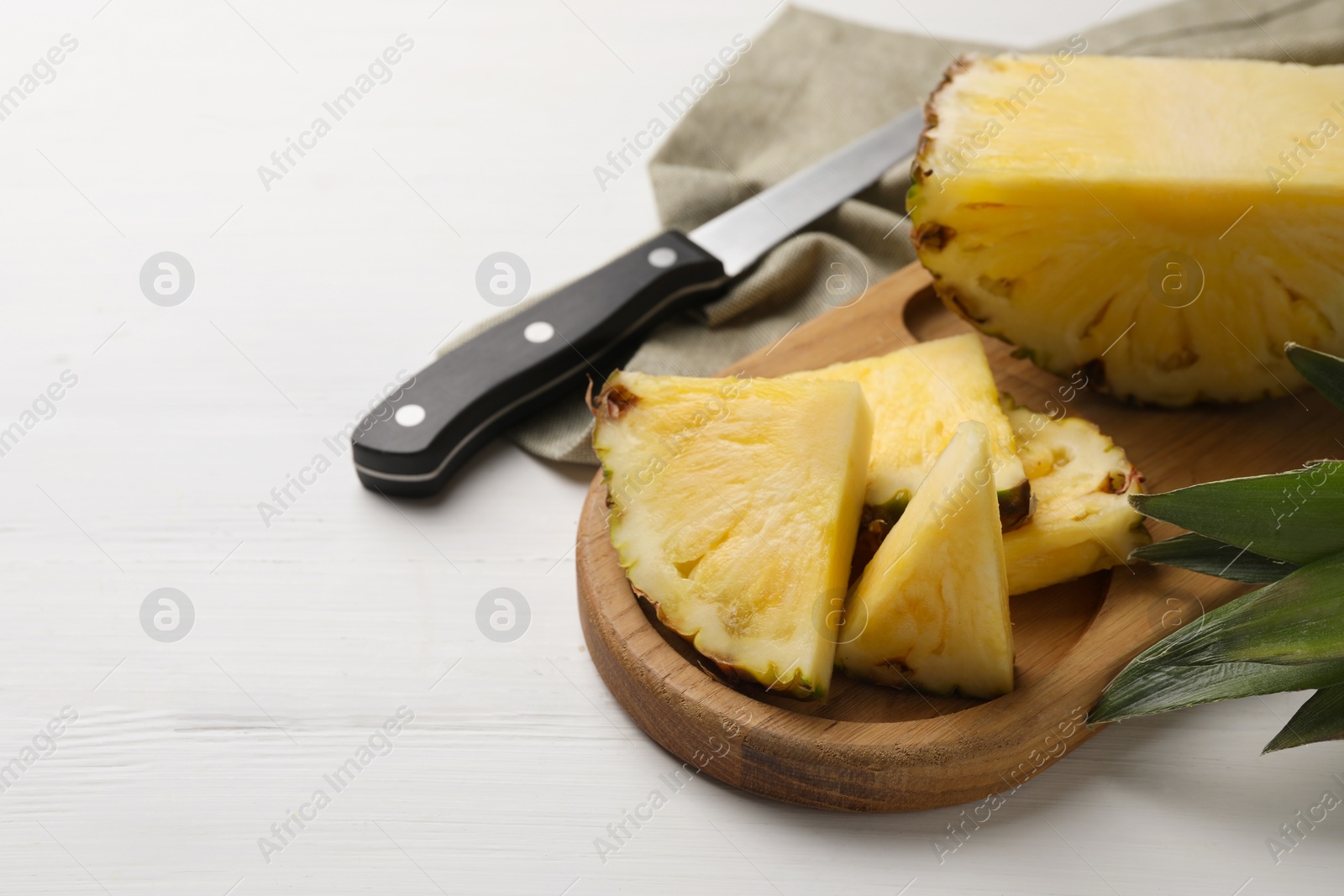 Photo of Slices of ripe juicy pineapple and knife on white wooden table, space for text