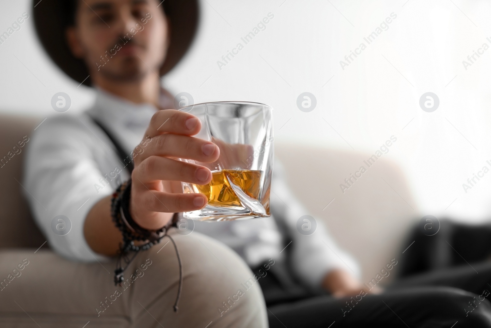 Photo of Young man with glass of whiskey sitting on sofa at home. Space for text