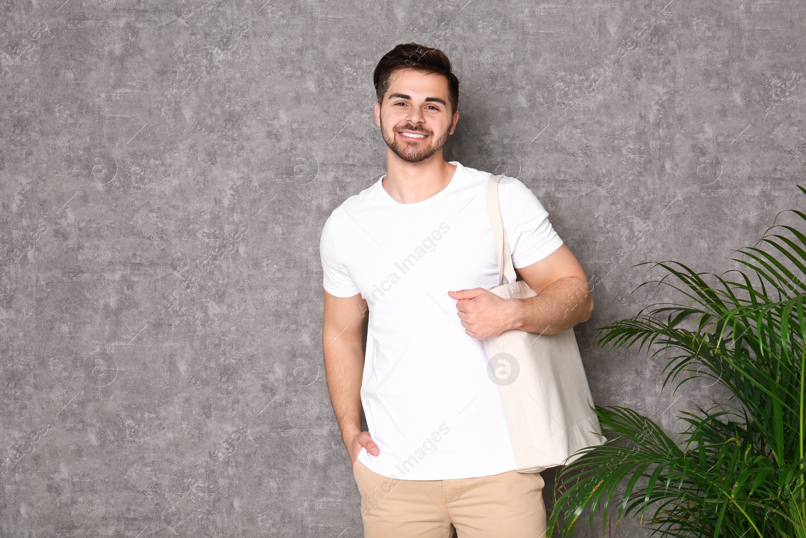 Photo of Portrait of young man with eco bag at indoor palm plant near grey wall