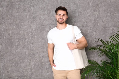 Photo of Portrait of young man with eco bag at indoor palm plant near grey wall