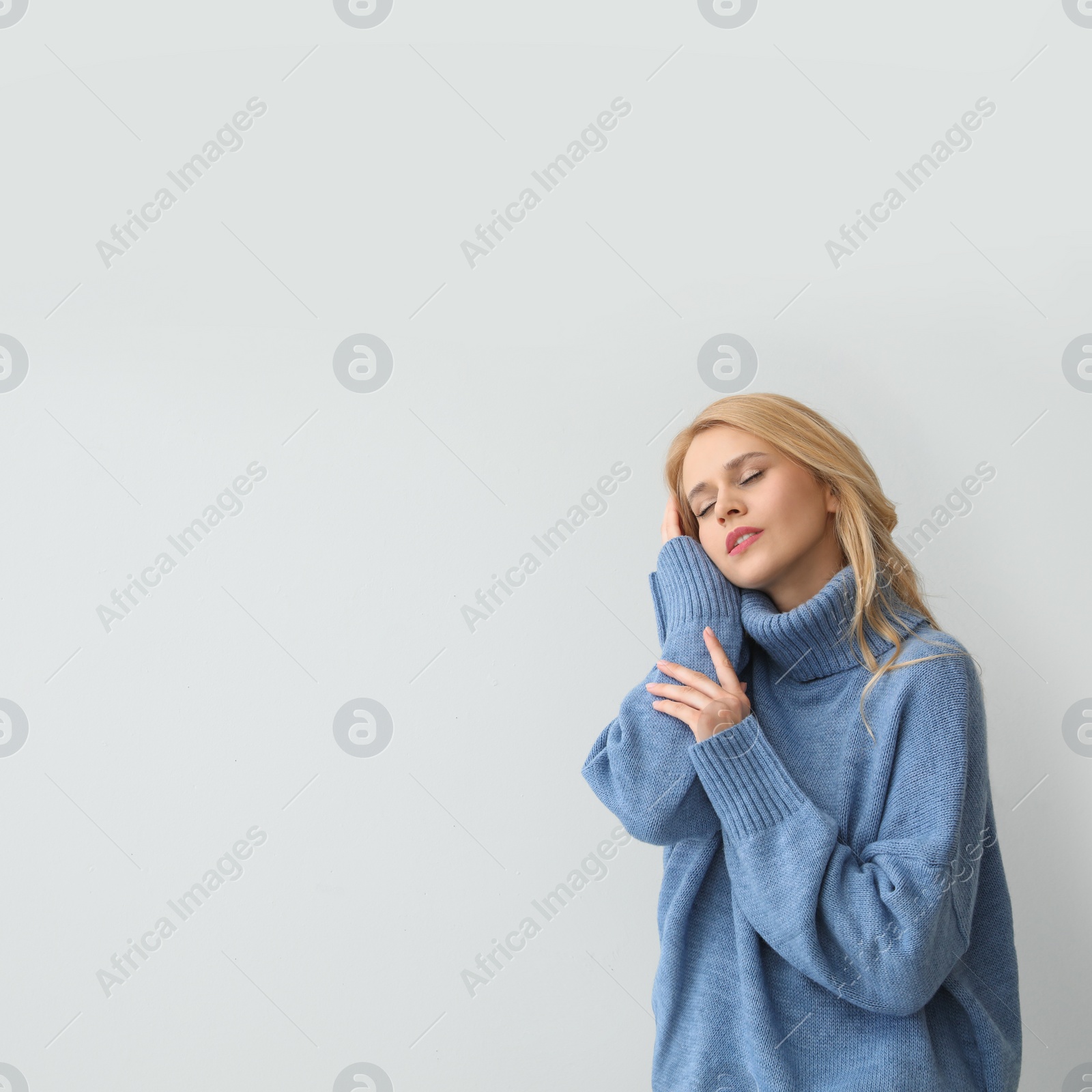 Photo of Beautiful young woman wearing warm blue sweater on light background. Space for text
