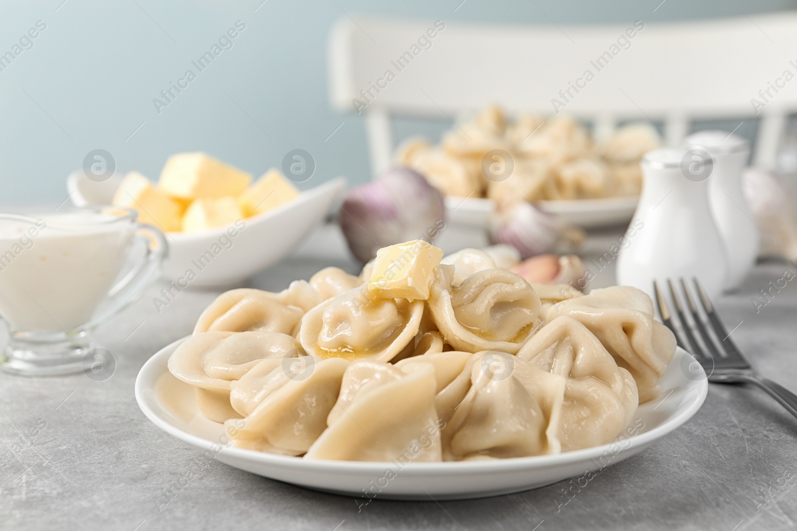 Photo of Tasty dumplings with butter on light grey table against blurred background