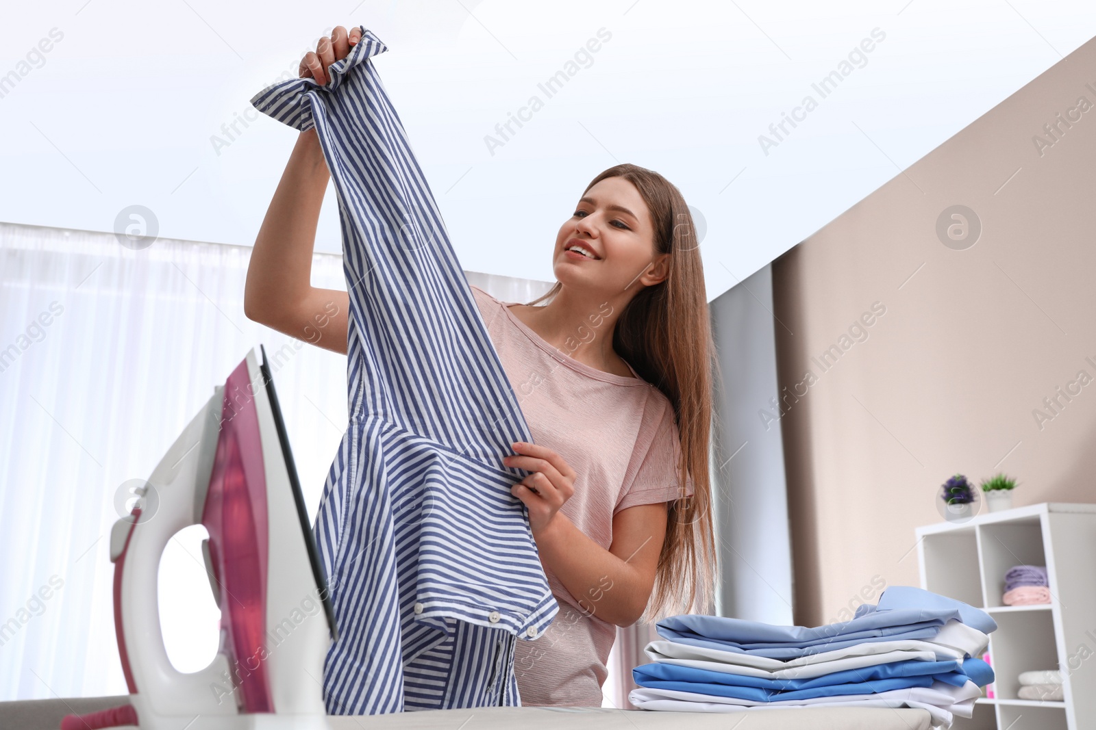 Photo of Young woman ironing clothes on board at home